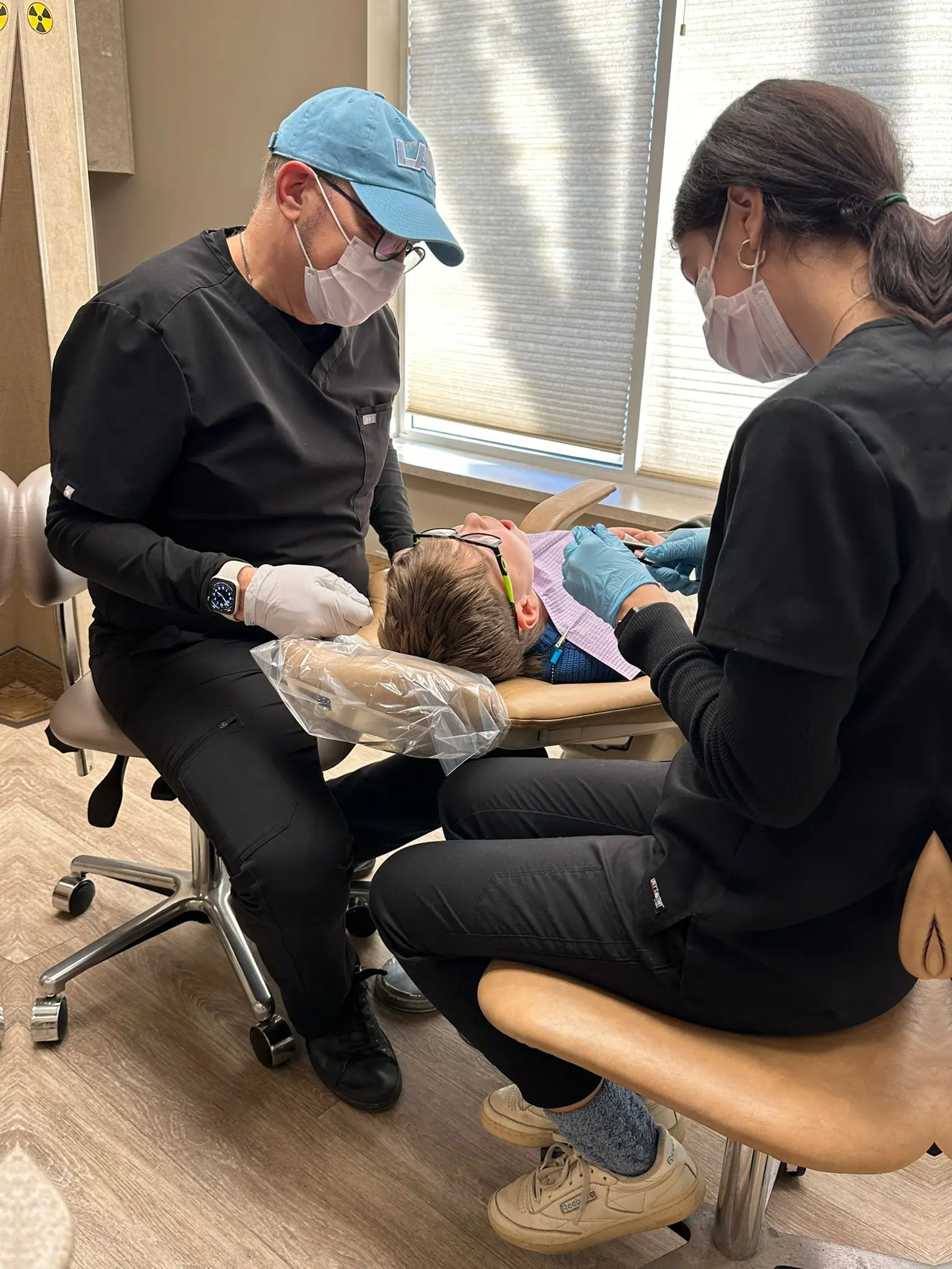 Two orthodontists examine a patient's teeth during a dental consultation in a clinical treatment room.